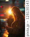 Backlit by the golden rays of the setting sun, a young woman walks through the city, focused on her smartphone amid warm evening tones 128130143