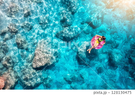 Aerial view of a young woman swimming with swim ring in blue sea 128130475