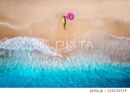 Aerial view of young woman with pink swim ring on the sandy beach 128130514