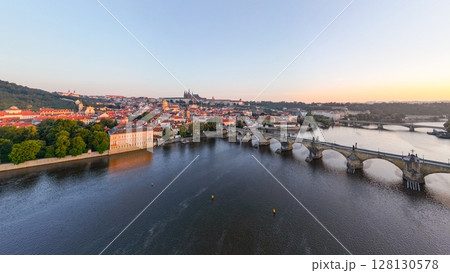 Bright colors fill the sky as the sun rises over Prague, illuminating the Vltava River and its medieval architecture. 128130578