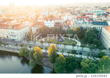 Visitors admire Kranner's Fountain surrounded by lush greenery in the Park of the National Awakening, overlooking the Vltava River and historic buildings of Prague during sunset. Visitors admire Kranner's Fountain surrounded by lush greenery in the Park of the National Awakening, overlooking the Vltava River and historic buildings of Prague during sunset. 128130583