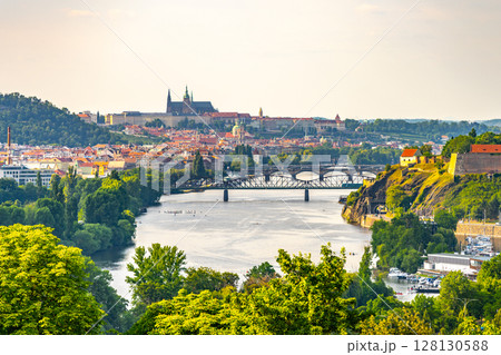 A breathtaking view of Prague showcasing the Vltava River winding through the city. The historic skyline features iconic landmarks, surrounded by lush greenery, creating a serene atmosphere. A breathtaking view of Prague showcasing the Vltava River winding through the city. The historic skyline features iconic landmarks, surrounded by lush greenery, creating a serene atmosphere. 128130588