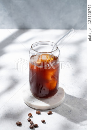Cold brew coffee in a glass with ice on a light concrete background with coffee beans 128130746