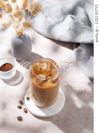 Ice latte coffee in a glass with milk on a light background with coffee beans, dry bouquet flowers 128130755