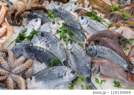 Bustling fish market in Greece displays abundant seafood like fresh fish, octopus, and various shellfish on ice, emphasizing local culinary traditions. 128130869