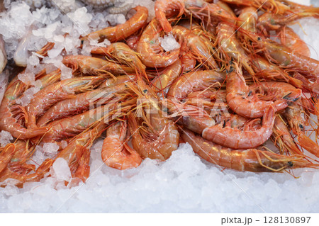 Vibrant fish market in Greece features fresh shrimps placed on ice, surrounded by seafood items. Vendors interact with customers while offering quality marine delicacies. Vibrant fish market in Greece features fresh shrimps placed on ice, surrounded by seafood items. Vendors interact with customers while offering quality marine delicacies. 128130897