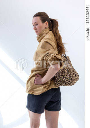 Elegant woman in beige windbreaker jacket and black shorts on light background. Fashionable female style. Studio photography. Vertical photo. High quality photo Elegant woman in beige windbreaker jacket and black shorts on light background. Fashionable female style. Studio photography. Vertical photo. High quality photo 128132454