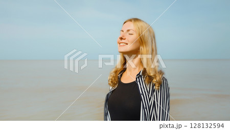 Calm relaxing young woman meditates, happy girl practicing breathing exercises on beach on sea 128132594