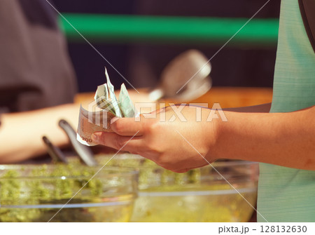 Person Holding Cash Against Culinary Background at Food Market Person Holding Cash Against Culinary Background at Food Market 128132630