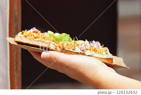 Hand Holding Gourmet Open-Faced Sandwich with Fresh Toppings on Cardboard Tray Hand Holding Gourmet Open-Faced Sandwich with Fresh Toppings on Cardboard Tray 128132632