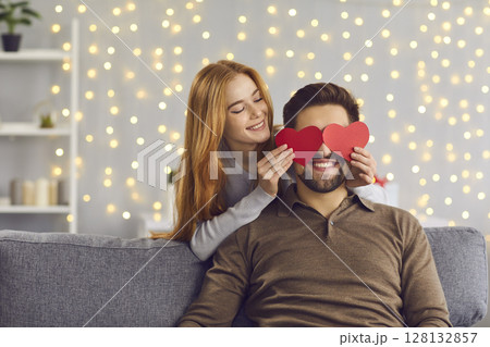 Woman covering boyfriend's eyes with red heart-shaped cards on Saint Valentine's Day Woman covering boyfriend's eyes with red heart-shaped cards on Saint Valentine's Day 128132857