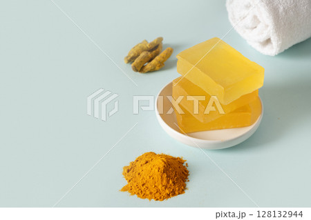 Handmade turmeric soap bars, powder and turmeric root on blue background. Organic skincare product perfect for wellness, beauty, and organic body care concepts. Close up. Copy space. 128132944