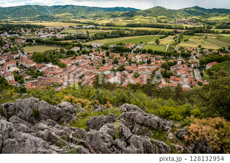 Picturesque View Of Vipava From Castle Ruins: Red-Tiled Rooftops And Church Tower Nestled In Green Valley With Blooming Flowers In Foreground And Rolling Fields In Background, Slovenia 128132954
