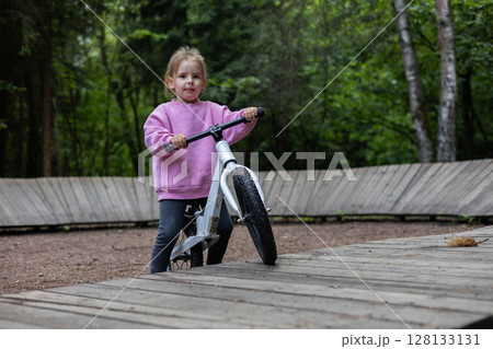 The child rides on a balance bicycle on the ramp located in the forest, enjoying events in the fresh air and developing his balance and coordination skills. The child goes on a bicycle on balancing. The child rides on a balance bicycle on the ramp located in the forest, enjoying events in the fresh air and developing his balance and coordination skills. The child goes on a bicycle on balancing. 128133131