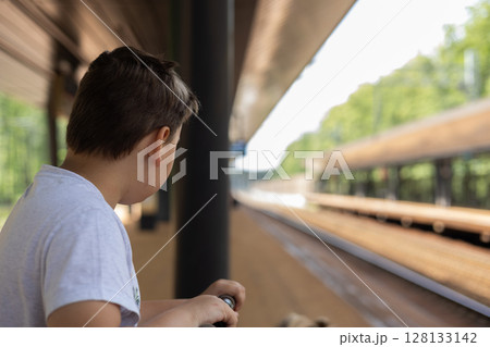 Young boy standing on a train platform, waiting for the train's arrival. Gripping the railing, gazing down the empty tracks at the quiet station, immersed in thoughts of adventure and anticipation. 128133142