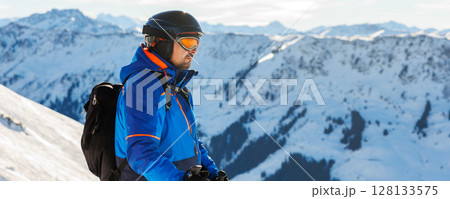 Young adult confident skier portrait at winter alpine skiing resort. Male sporty person with backpack mountain Alps snow slope outdoors cold snowy day 128133575