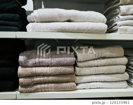 White and tan stack of towels sits on a shelf next to a black stack White and tan stack of towels sits on a shelf next to a black stack 128133961