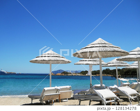 Escape to the stunning shores of Sardinia with these vibrant stock photos capturing the essence of Mediterranean tranquility. Featuring a pristine beach lined with straw umbrellas, sun loungers, and 128134278