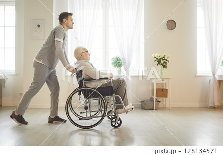 Nurse in uniform pushing disabled male senior patient in wheelchair in medical clinic Nurse in uniform pushing disabled male senior patient in wheelchair in medical clinic 128134571