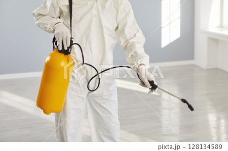 Exterminator service man, worker wearing protective white coverall holding pump sprayer  128134589