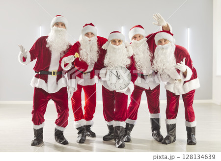 Happy funny male people in Santa Claus red costumes holding clock showing five minutes to midnight Happy funny male people in Santa Claus red costumes holding clock showing five minutes to midnight 128134639