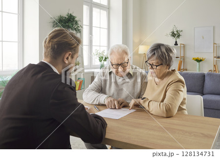 Senior couple sitting at table and studying terms of health insurance contract with financial agent. 128134731