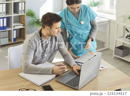 Man doctor and female nurse helping with doing paper work, discussing results of patients tests Man doctor and female nurse helping with doing paper work, discussing results of patients tests 128134817