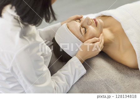 Beautician applying anti-aging facial cream on woman client face in spa salon. 128134818