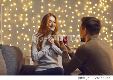 Man in love kneels in front of a girl with a wedding ring in his hands and offers her marriage. Man in love kneels in front of a girl with a wedding ring in his hands and offers her marriage. 128134962
