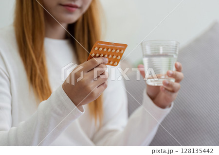 Young Woman Holding Birth Control Pills and a Glass of Water, Concept of Contraception and Family Planning 128135442