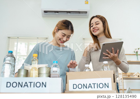 Two Women Organizing donate in Boxes with Labeled Signs in a Bright Room Two Women Organizing donate in Boxes with Labeled Signs in a Bright Room 128135490