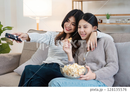 Happy LGBT Couple Relaxing at Home, Watching TV and Enjoying Popcorn Together in a Cozy Living Room Setting, Embracing Love and Togetherness, Celebrating Modern Lifestyle and Inclusivity 128135576