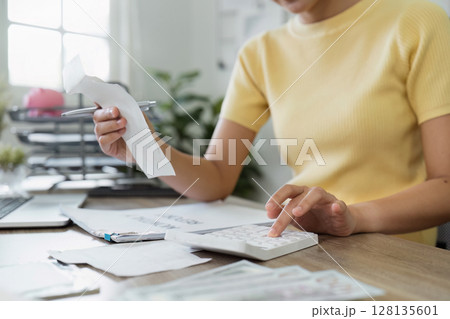 Young Woman Calculating Expenses at Home Office Desk for Financial Planning and Budgeting with Calculator, bills, and Documents Young Woman Calculating Expenses at Home Office Desk for Financial Planning and Budgeting with Calculator, bills, and Documents 128135601