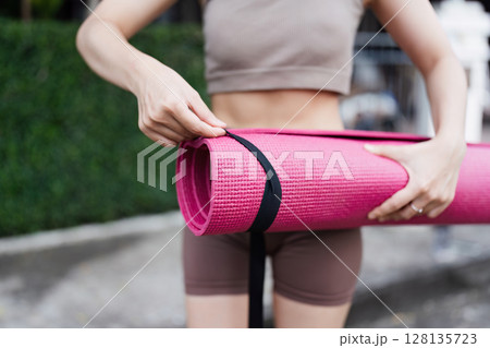 Woman Preparing for Yoga Session Outdoors with Pink Mat, Emphasizing Fitness and Wellness in a Natural Setting, Ideal for Promoting Healthy Lifestyle and Mindfulness Practices 128135723