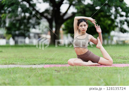Young Woman Practicing Yoga Outdoors in a Park, Demonstrating Flexibility and Balance in a Natural Setting, Promoting Health and Wellness Through Mindful Exercise and Meditation 128135724