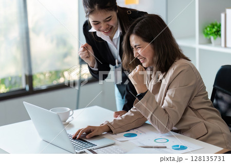 Professional Business Team Celebrating Success in Modern Office Environment with Laptops and Financial Charts Professional Business Team Celebrating Success in Modern Office Environment with Laptops and Financial Charts 128135731