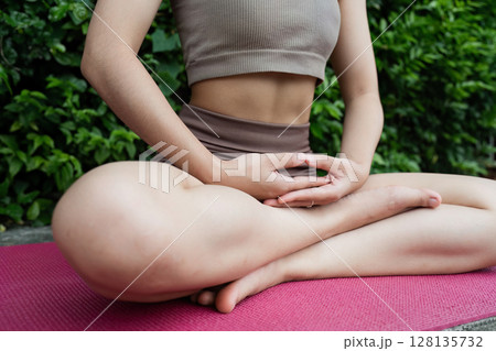 Serene Yoga Practice Outdoors Woman Meditating in Lotus Pose on a Yoga Mat in a Green Natural Setting for Wellness and Mindfulness 128135732