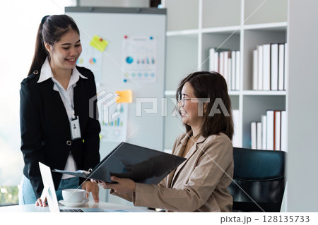 Professional Business Meeting in Modern Office Setting with Two Female Colleagues Discussing Documents and strategy Professional Business Meeting in Modern Office Setting with Two Female Colleagues Discussing Documents and strategy 128135733