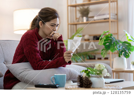 Young Woman Analyzing Bills at Home, management Finances, and Banking Online in a Modern Living Room Setting 128135759