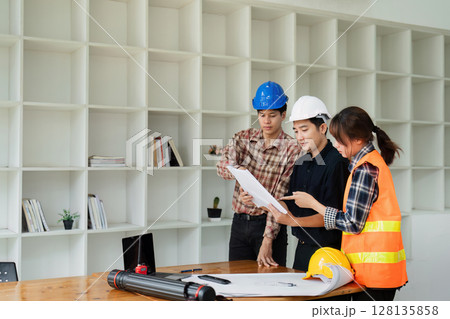 Team of Engineers and Architects Collaborating on Construction Project in Modern Office with Shelves in Background 128135858