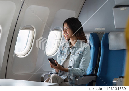 Businesswoman on Airplane Using Smartphone, Comfortable Business Class Travel, Modern Air Travel, Professional Woman, In-flight Connectivity, Corporate Travel, Business Trip, Efficient Travel 128135880