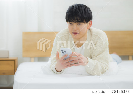 ベッドでスマホを使う若い男性 128136378