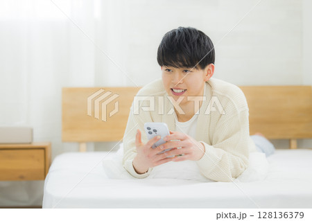 ベッドでスマホを使う若い男性 128136379