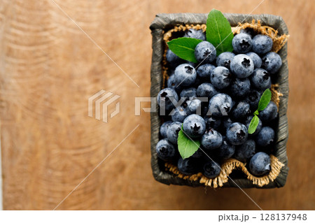 Ripe blueberries in wicker basket on wooden table. 128137948