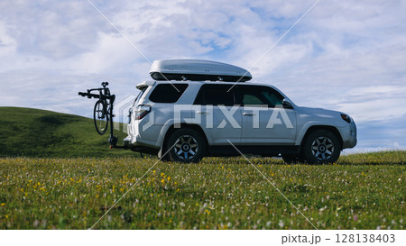 Offroad car carrying bikes on flowering grassland mountain under blue sky Offroad car carrying bikes on flowering grassland mountain under blue sky 128138403