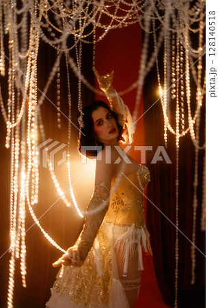Young woman in vintage corset costume posing under chandelier on dark background 128140518