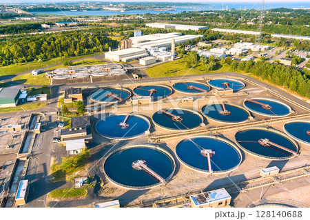 Aerial view of wastewater treatment plant with circular tanks, machinery, nearby greenery 128140688