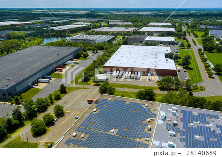 Solar panels on rooftops several warehouses in lush industrial area captured on sunny day. 128140689