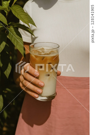 Woman in white top and pink skirt holds refreshing iced latte 128141905