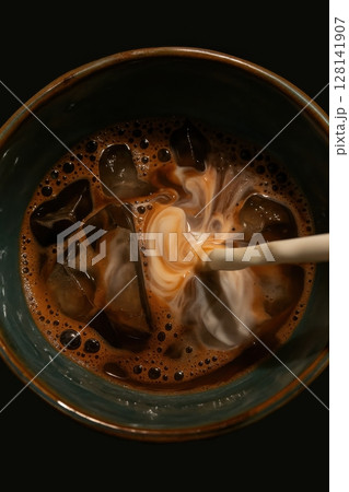 Close-up of iced coffee in a ceramic cup with swirling cream 128141907
